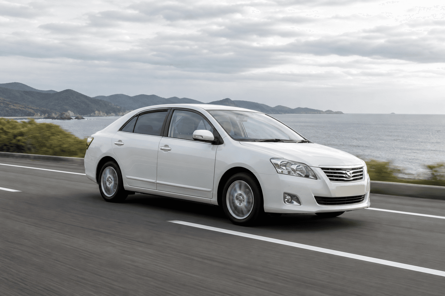 Pearl white Toyota Allion sedan on a coastal highway